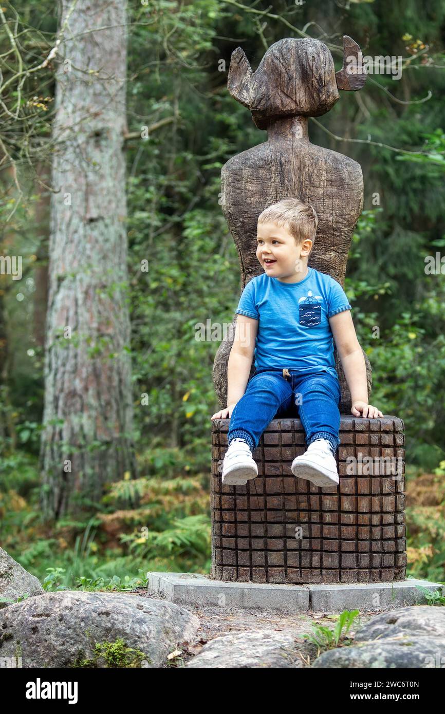 Portrait of a little cheerful boy sitting on a witch's throne in the forest. Vertical photo. Stock Photo