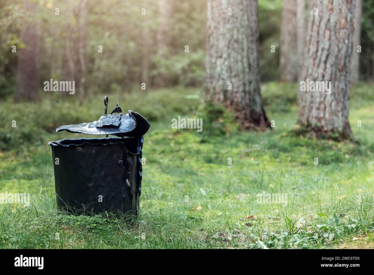 Artistic iron garbage bin, black trash can in the forest. metal