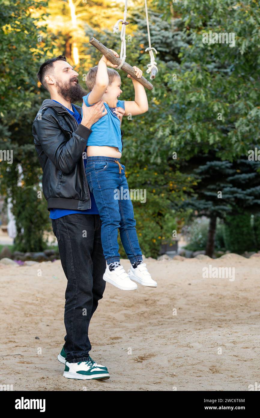 Father and son playing on outdoor swing park. Happy family, closeness of father and son. Stock Photo