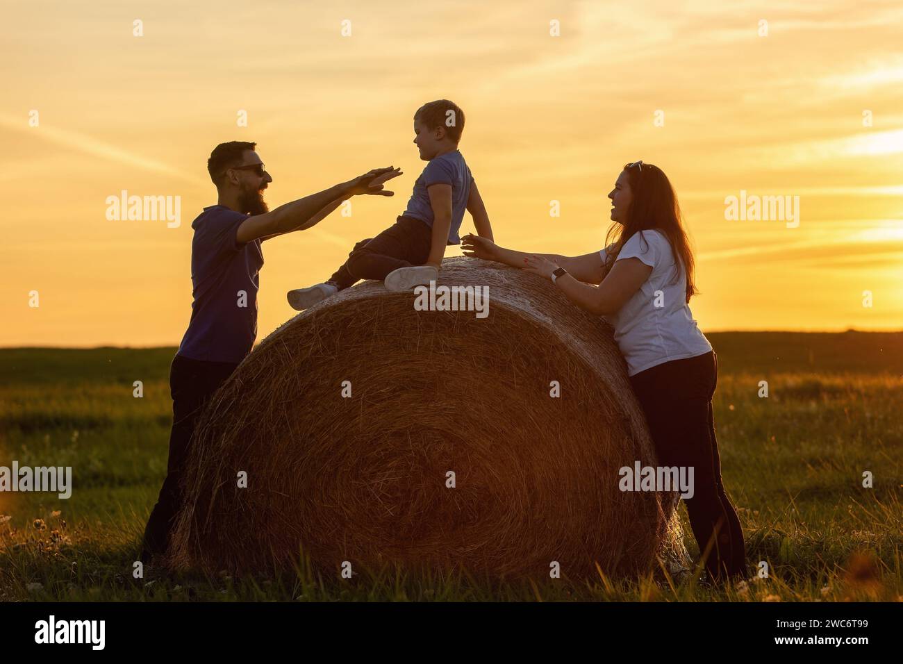 A happy family playing on a straw roll in the golden evening light. Stock Photo