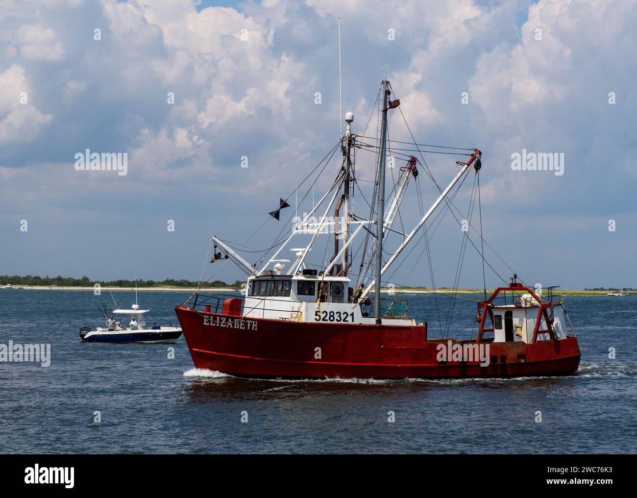 A vibrant red fishing boat gracefully glides along the calm waters of a picturesque river Stock Photo