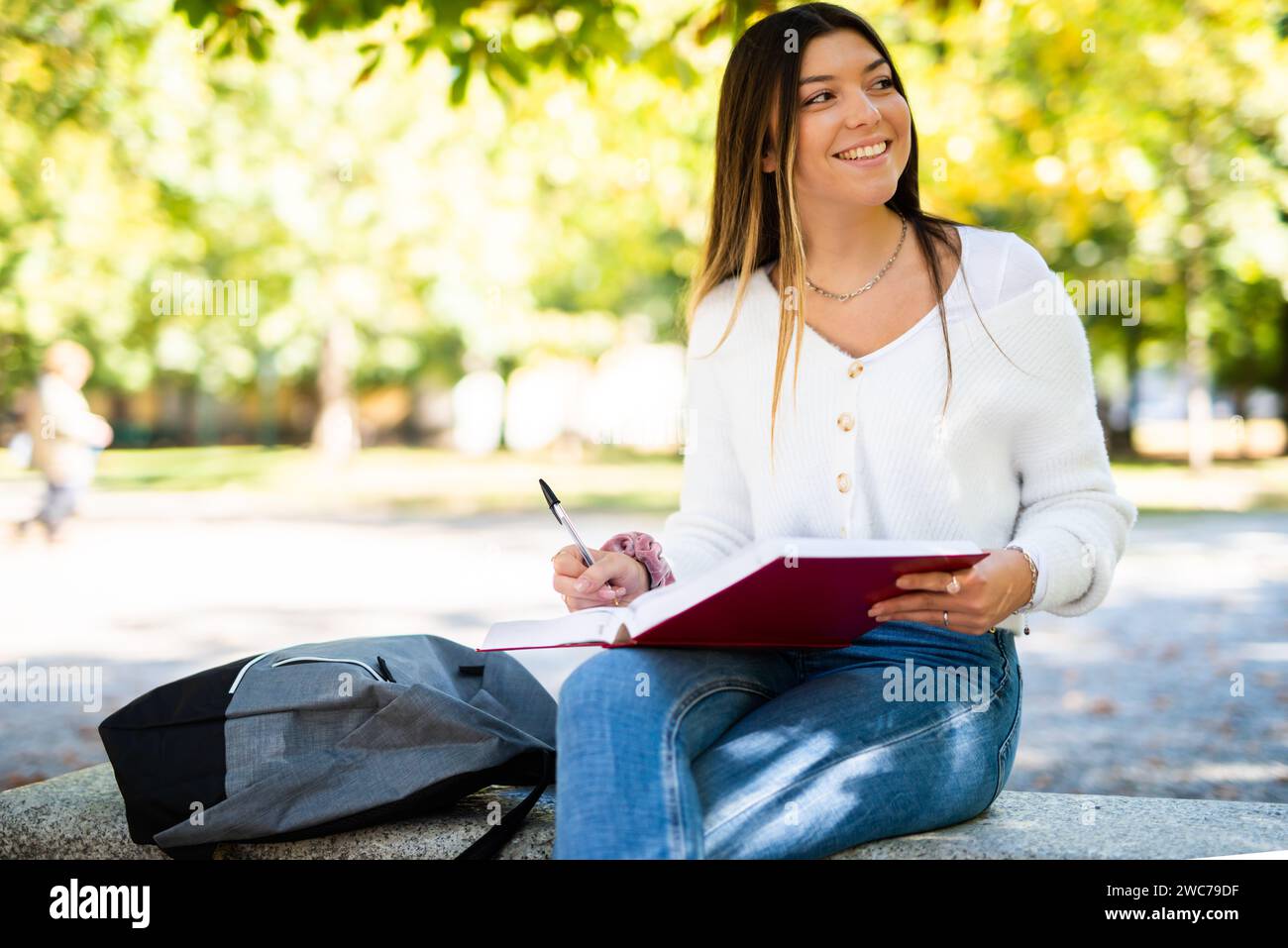 Beautiful female college student reading a book on a bench in a park Stock Photo