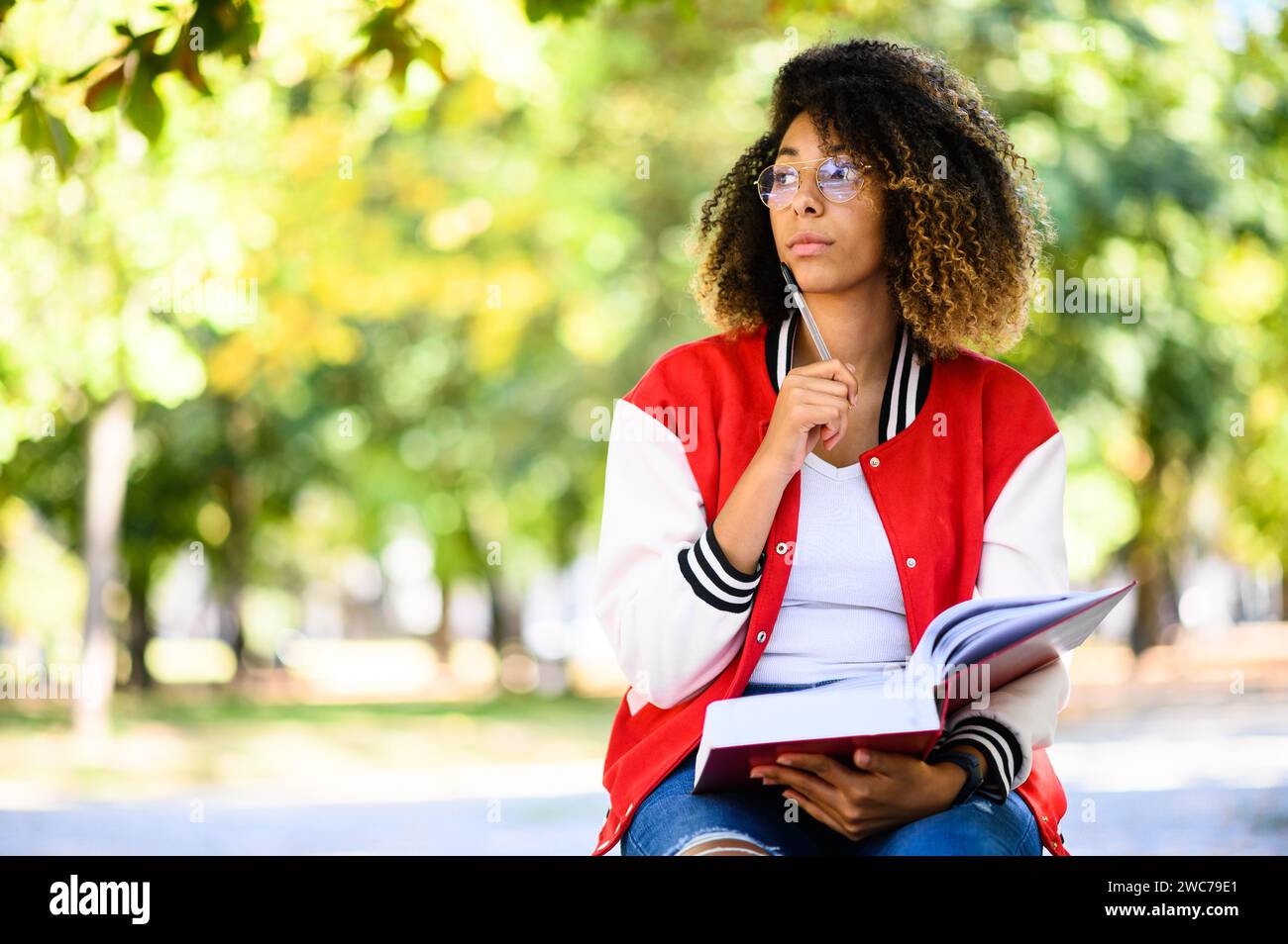 Beautiful african female college student reading a book on a bench in a park Stock Photo