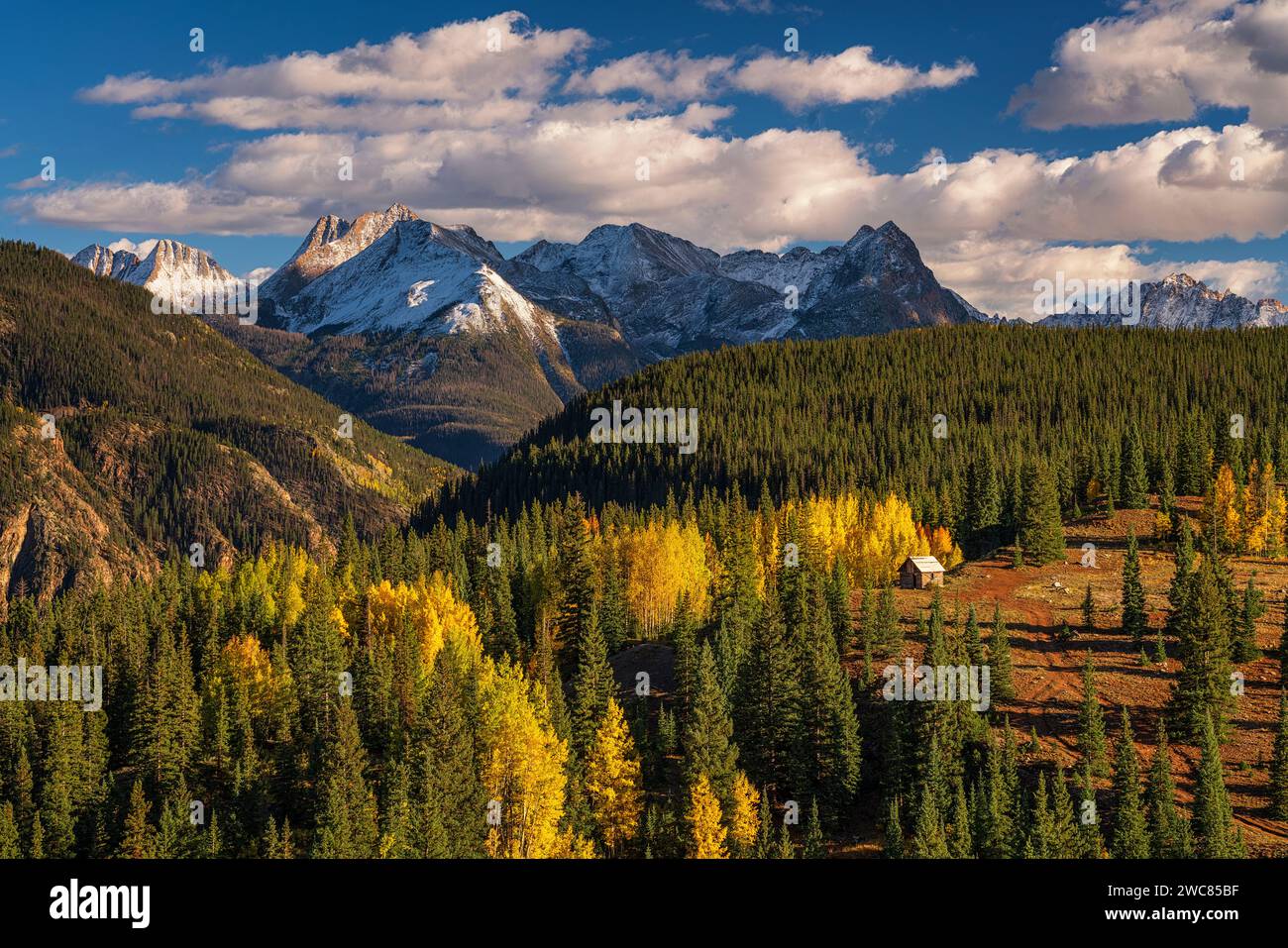 Mining shack nestled in aspens and pine forest beneath snow-covered mountains along the Million Dollar Highway in Colorado Stock Photo