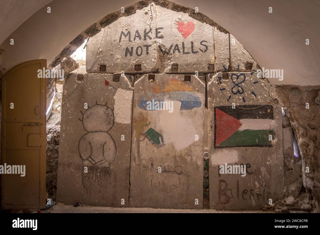 The concrete barricades at Hebron Old City with Palestinian flag, words 'make love not war' and murals, on the bo Stock Photo