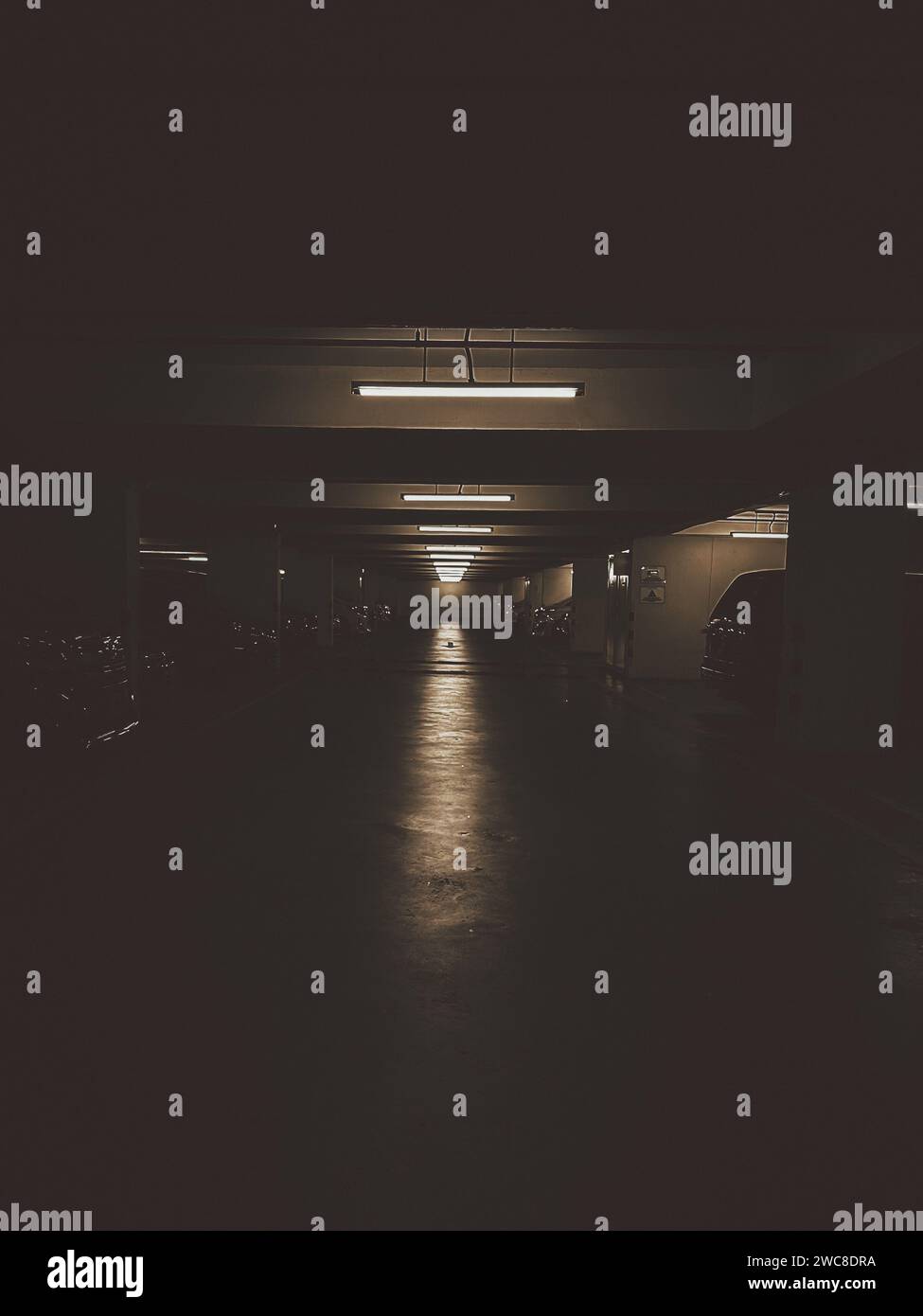 The dimly lit empty parking garage exudes a grunge atmosphere with its worn-out asphalt. Stock Photo