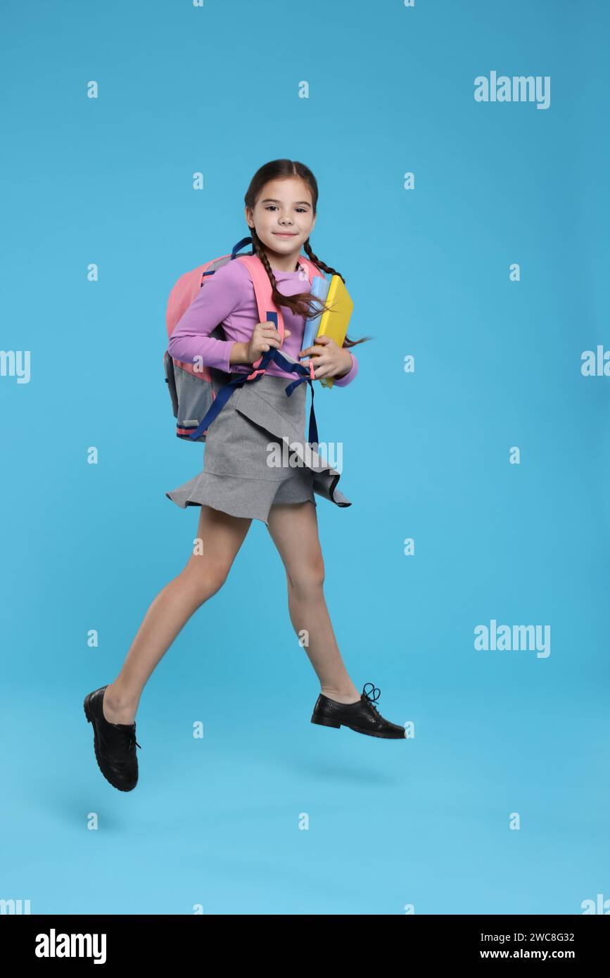 Cute schoolgirl holding books and jumping on light blue background ...