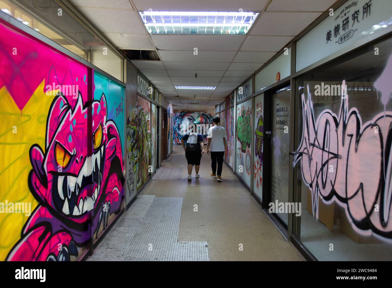 Two guys walked down the shopfronts that is painted in graffiti work for art community purpose, tenants had moved out at Peace Centre Singapore. Stock Photo