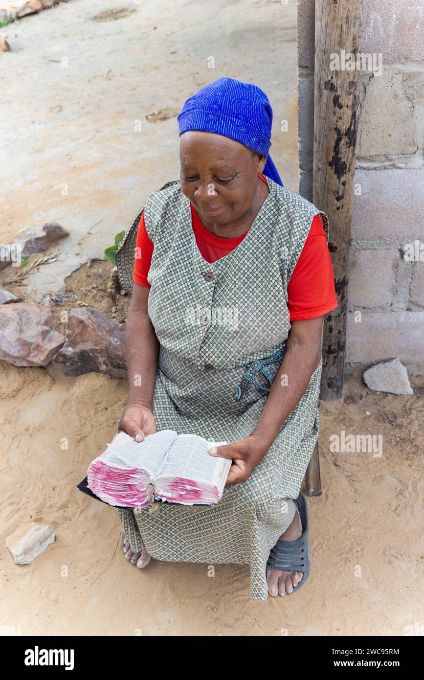 old african woman reading the bible in the yard, village in Botswana Stock Photo