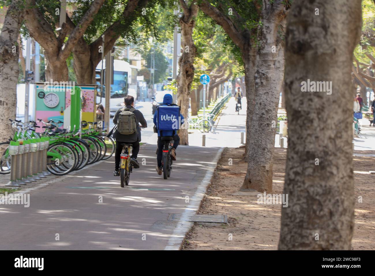 A cyclist and a delivery boy riding on a bike path in the city. The riders are photographed from behind Stock Photo