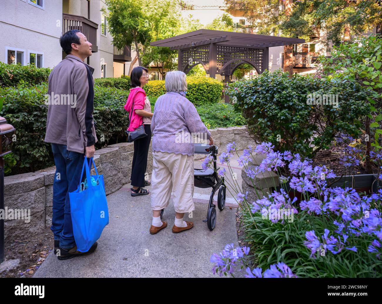 Elderly woman walking using a mobility walker in the retirement village, accompanied by her family. Stock Photo