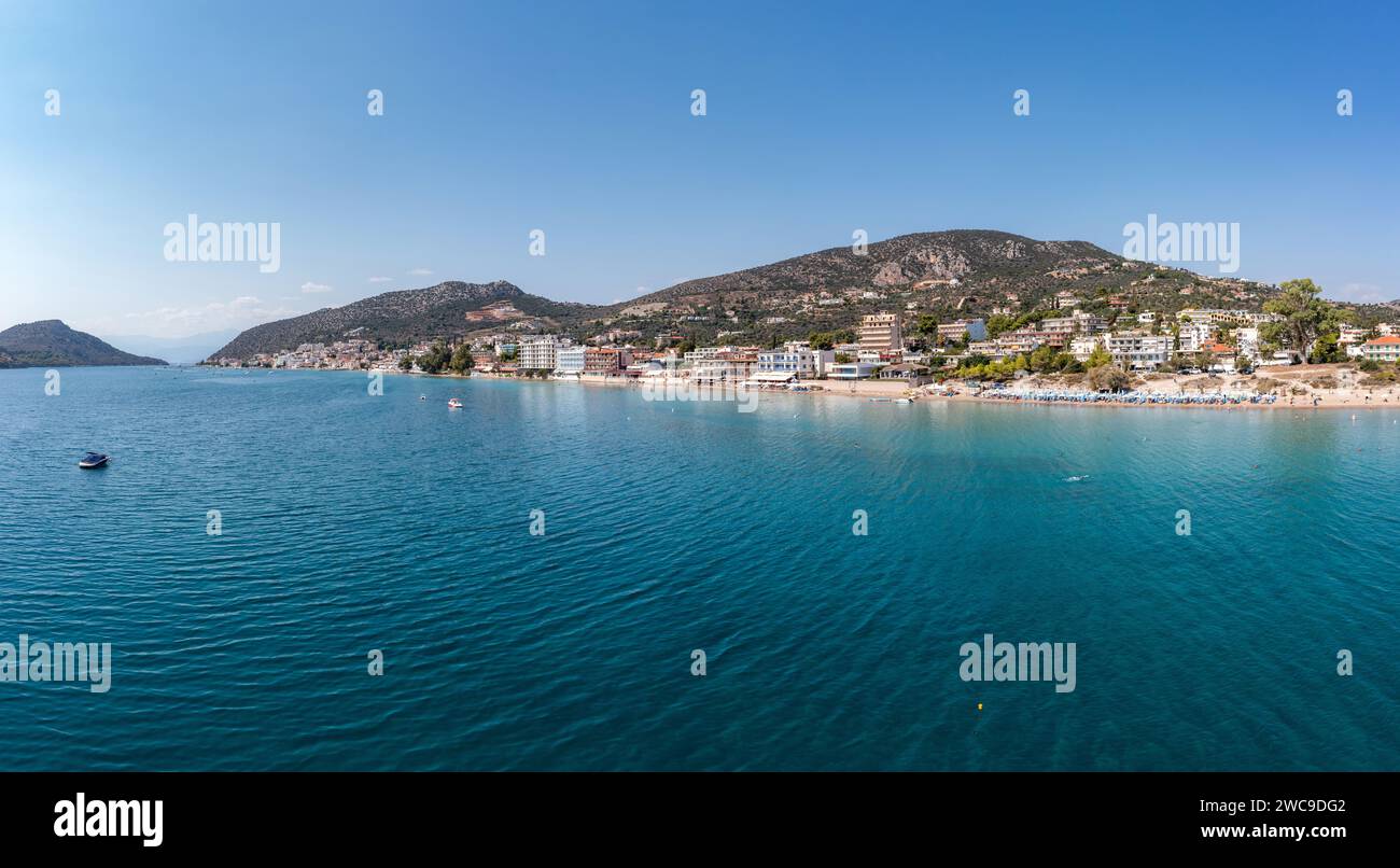 Greece, Tolo near Nafplio, Argorida, Peloponnese. Aerial drone panoramic view of village, moored boat in ripple sea water, blue sky background. Space Stock Photo
