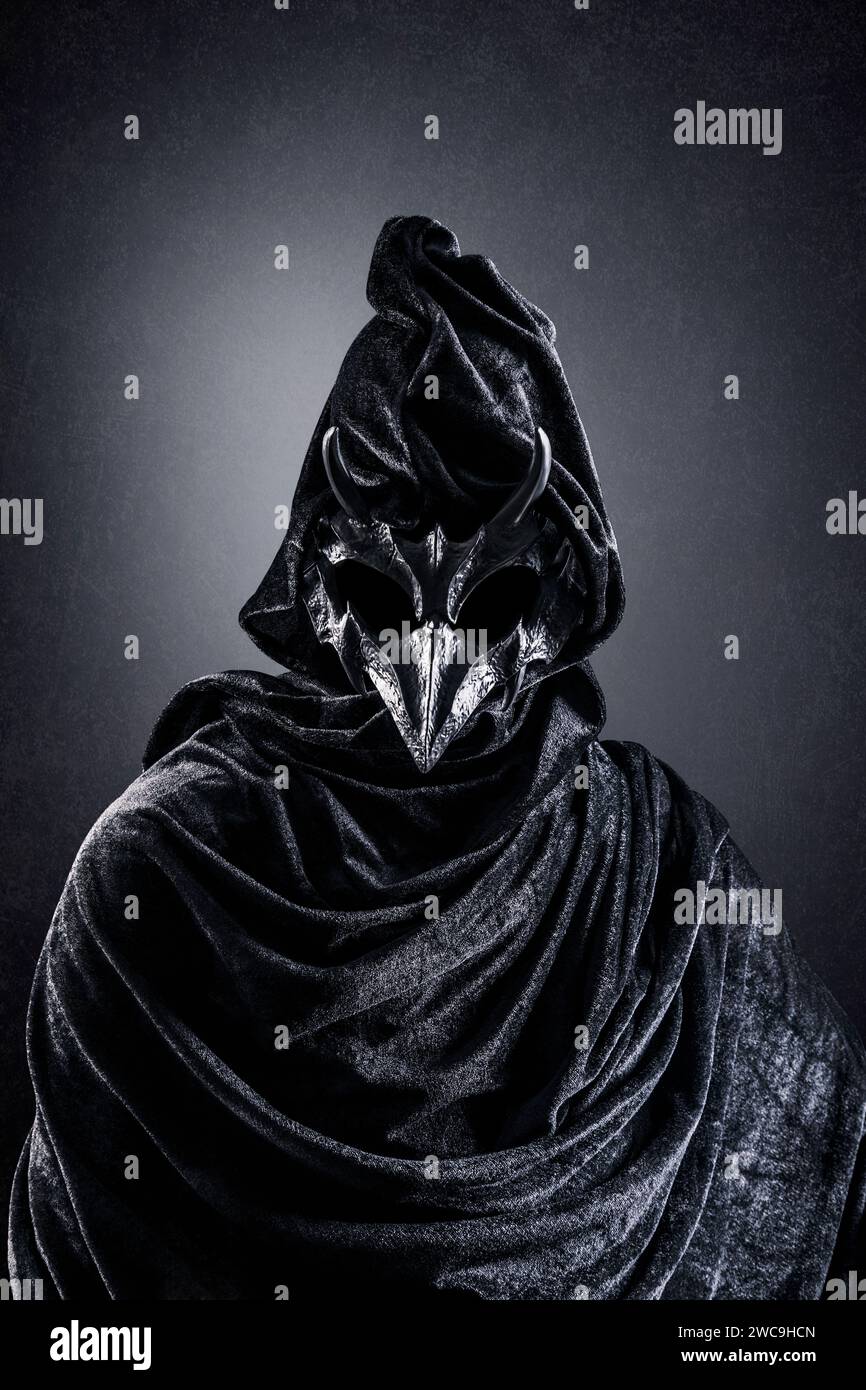 Creepy figure with animal horned skull over dark misty background Stock Photo