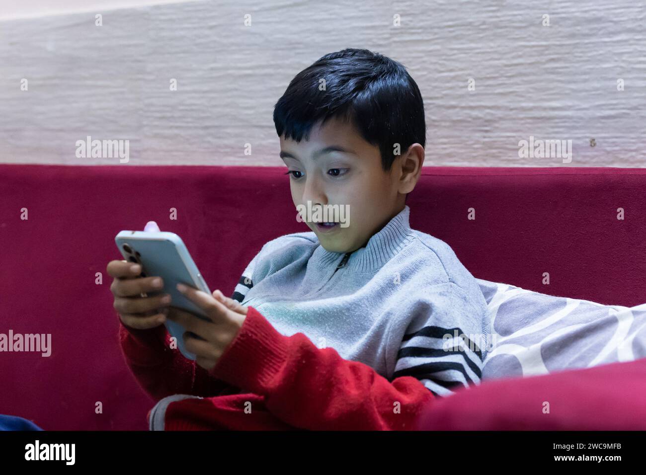 young kid facial expression while watching mobile and playing online game at home at night Stock Photo