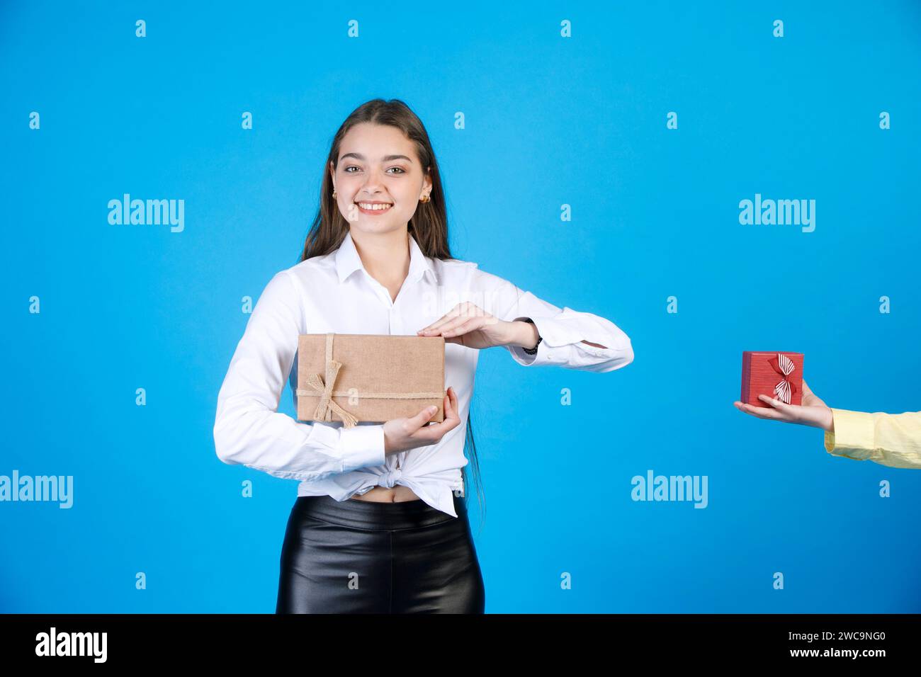 Cheerful lady holding gift box, unfolding it, while looking at camera, with anonymous hand beside. Stock Photo