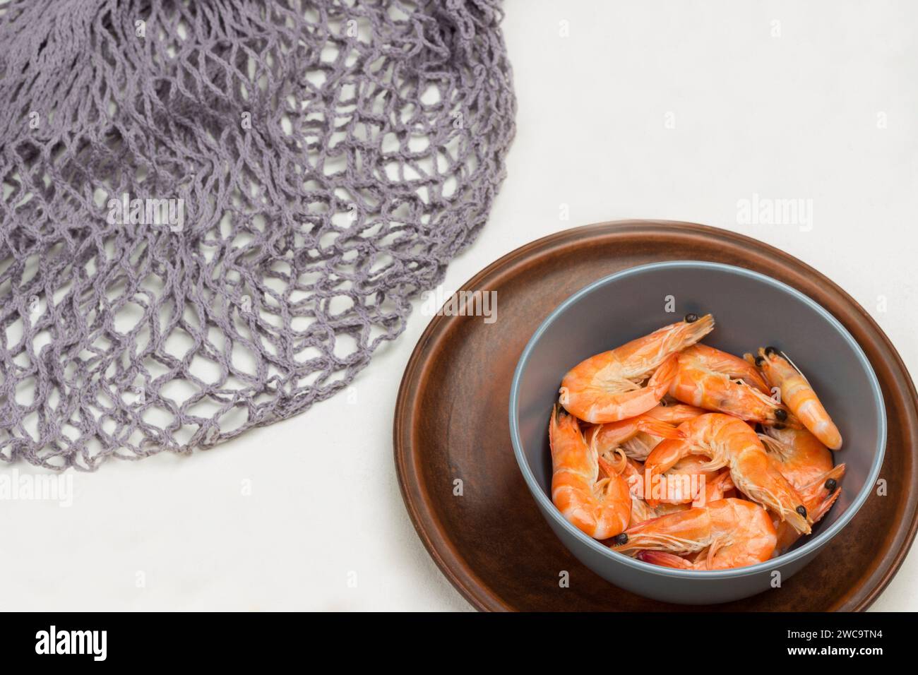 Shrimp in gray bowl. Gray mesh, allspice and lemon on table. White background. Top view Stock Photo