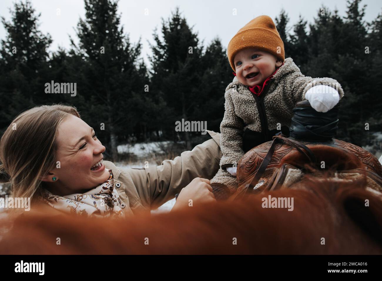 Mom happily holds baby boy on horseback adventure Stock Photo