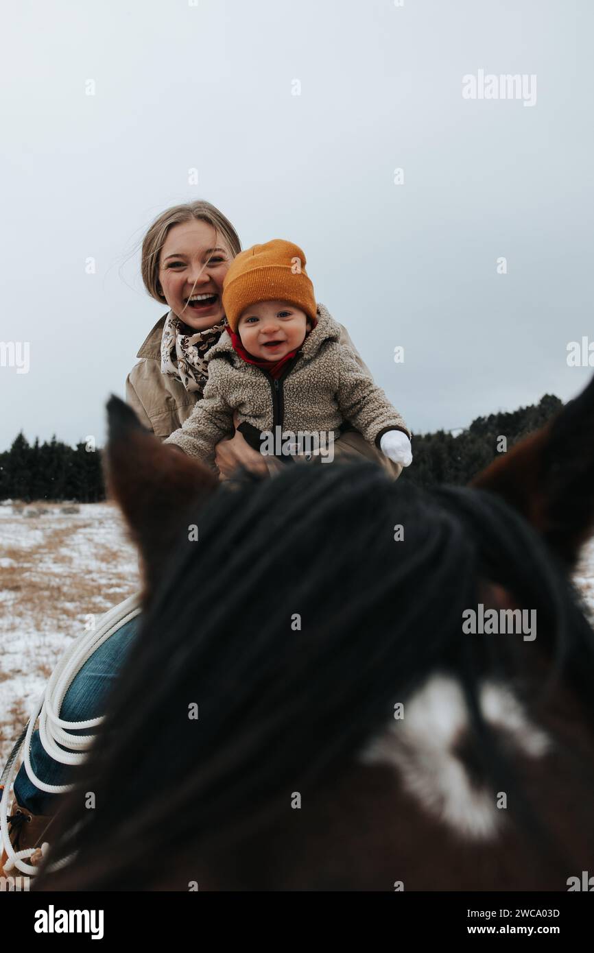 Mom holds baby on horse, savoring their joyous ride Stock Photo