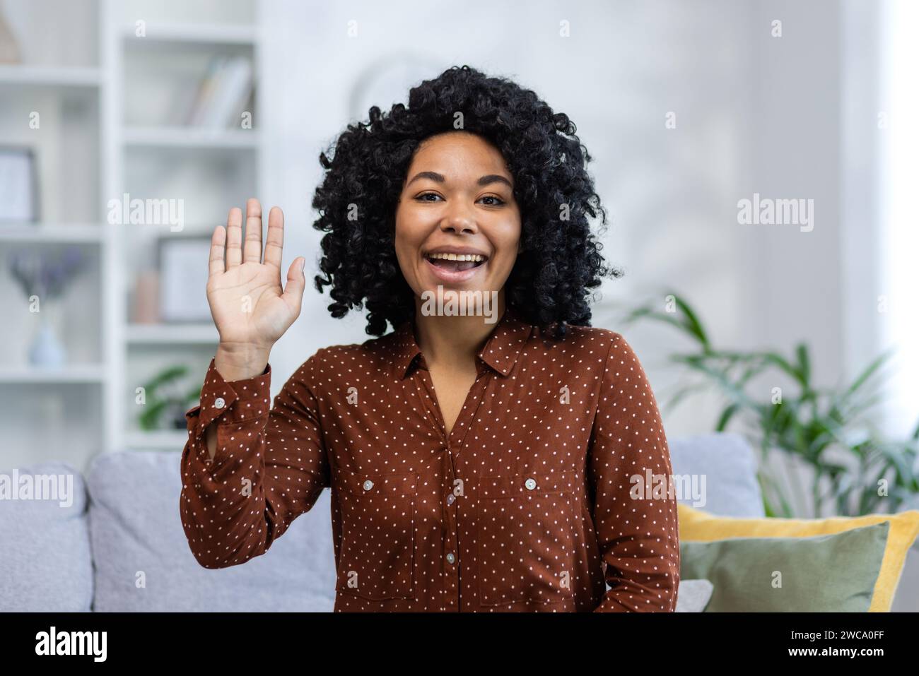 Close-up portrait of a young African American woman greeting, waving and talking to the camera. Stock Photo