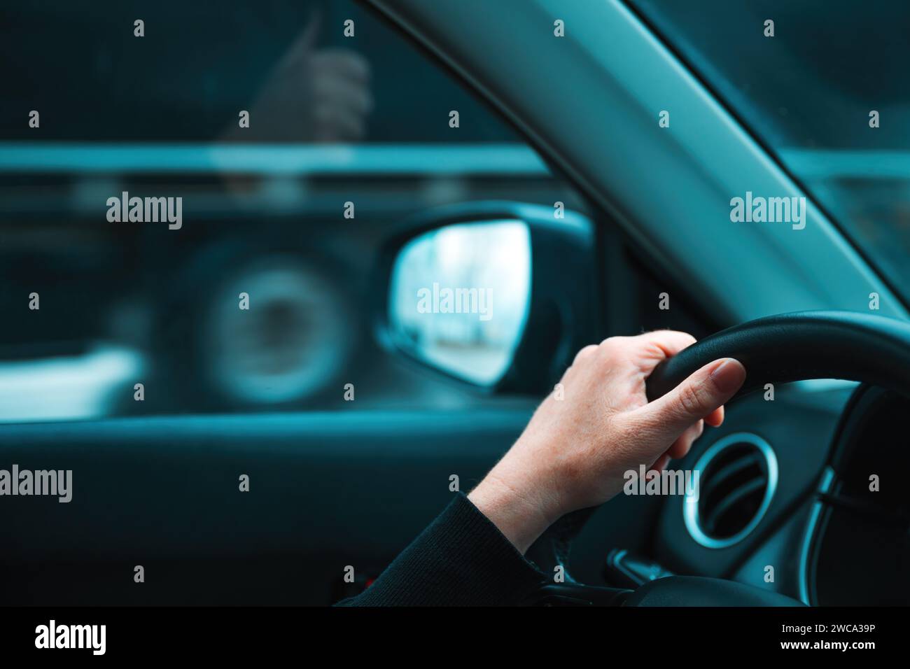 Getting away from it all concept, closeup of female hand on car steering wheel, woman driving vehicle along the road and passing by semi-truck, select Stock Photo