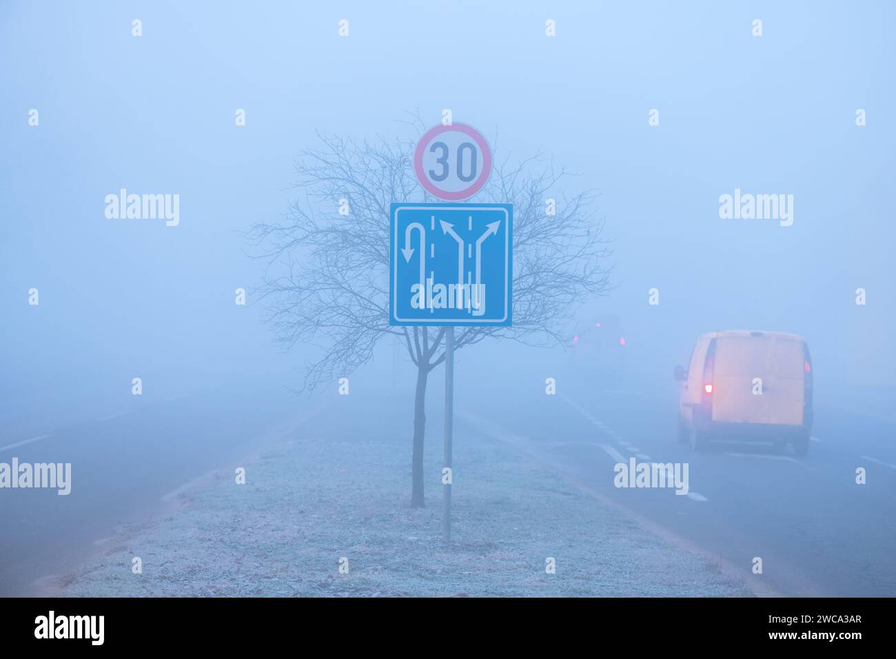 Traffic in fog, road signs and vehicle on the road, selective focus Stock Photo