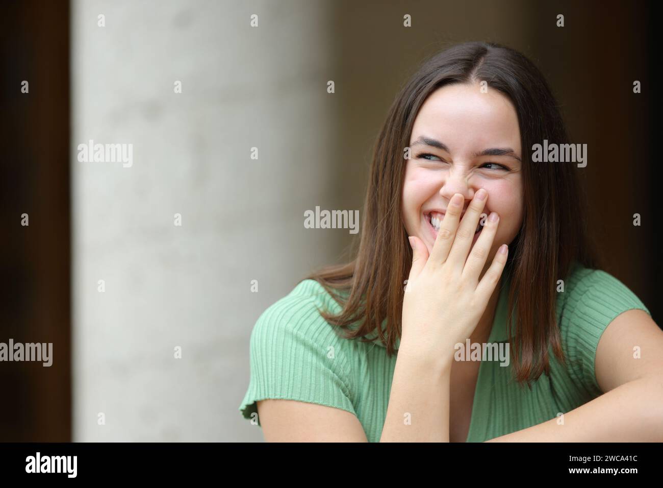 Front view portrait of a happy woman laughing hiding mouth with hand in the street Stock Photo