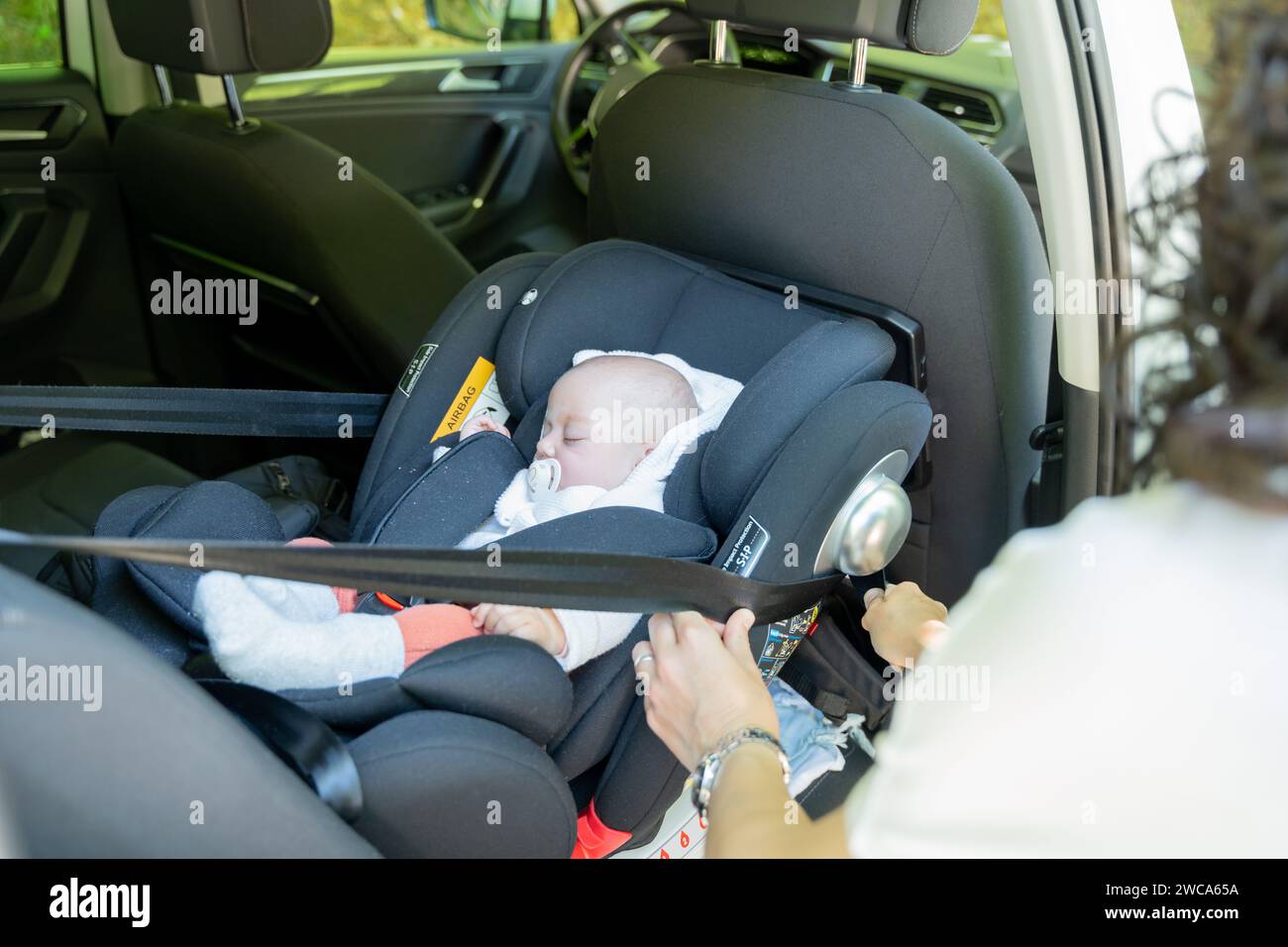 young mother adjusting the seat belt of her baby's transport seat in the car, child restraint system in the vehicle. safety concept in child transport Stock Photo