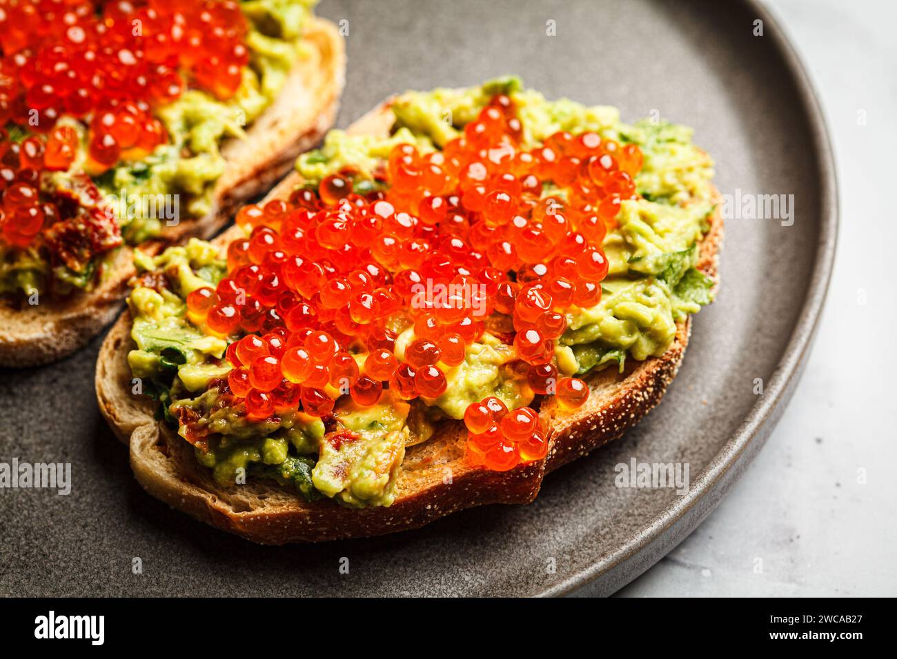 Red caviar and avocado guacamole toast with rye bread, close-up, . Stock Photo