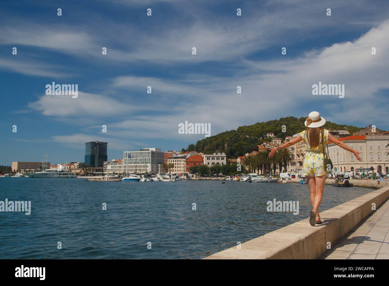 a young attractive woman in a hat walks along the waterfront in Split, Croatia Stock Photo
