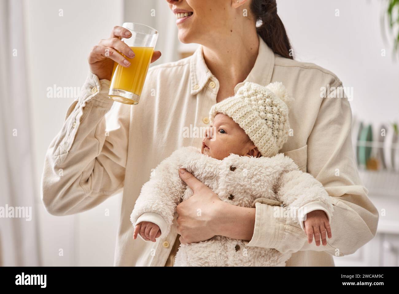 cheerful loving mother holding her newborn baby boy and drinking orange