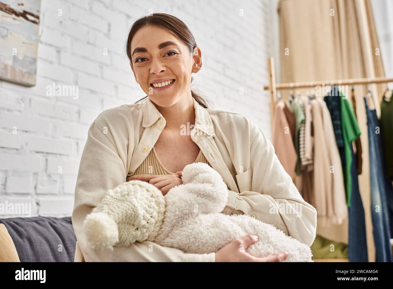 attractive caring jolly mother in cozy homewear breastfeeding her newborn child, modern parenting Stock Photo