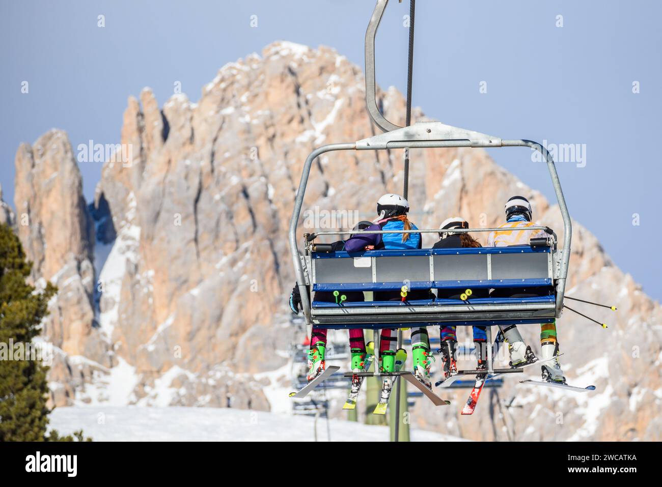Skiers riding a chairlift in a mountain resort in winter. a Snowy rocky peak is in background. Stock Photo