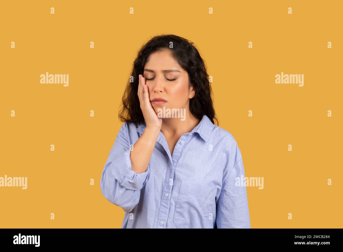 Woman with a pained expression, hand on her cheek, eyes closed, possibly suffering from a toothache Stock Photo