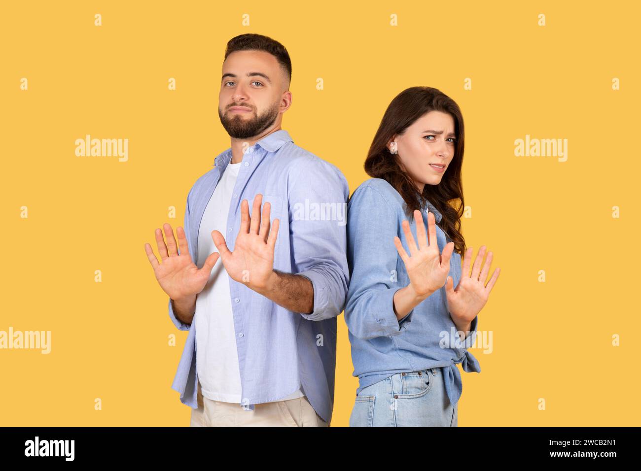 Couple gesturing stop with hands, standoffish poses, yellow background