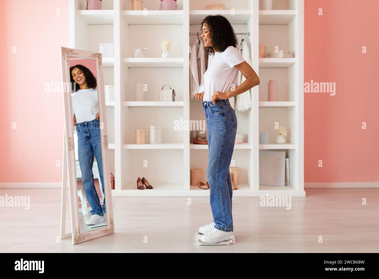 Young woman in jeans checking fit in mirror, pink room Stock Photo - Alamy