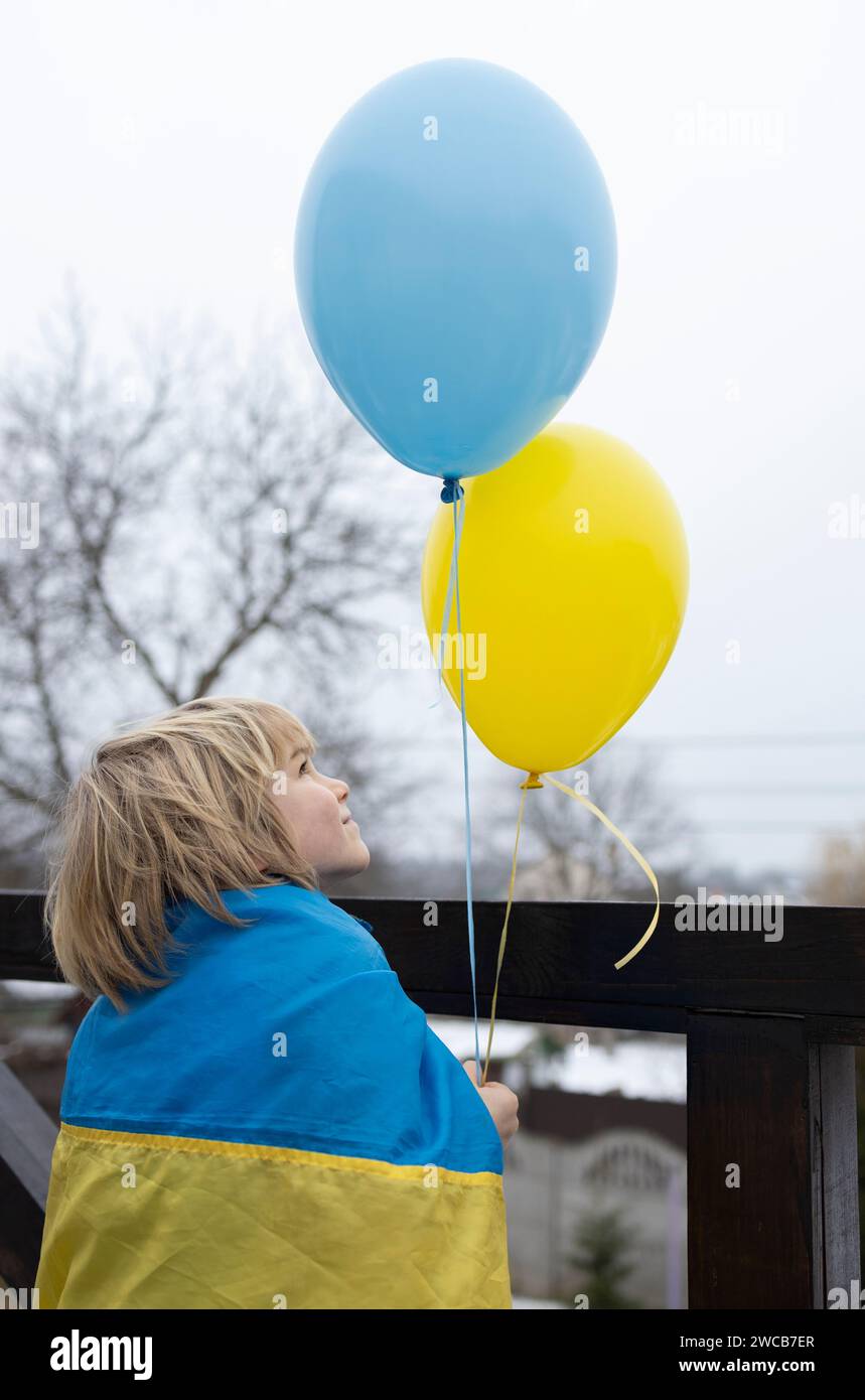 boy wrapped in a Ukrainian flag with yellow and blue balloons. faith in victory. nostalgia for homeland Ukraine. Patriotic concept. Stand with Ukraine Stock Photo