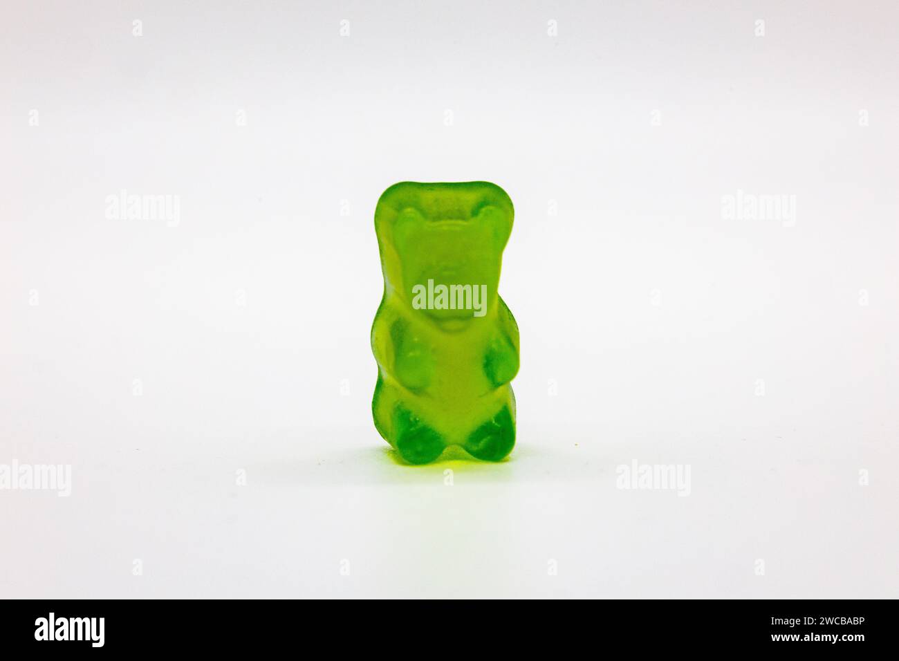 A colorful gummy bear is placed on a vibrant apple green tablecloth, creating a playful and eye-catching composition Stock Photo
