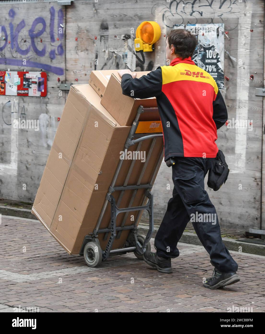 Ein Paketbote transportiert in Freiburg mit einer Karre Pakete . DHL-Paketzustellung in der Vorweihnachtszeit in Freiburg. *** A parcel carrier transports parcels in Freiburg with a trolley DHL parcel delivery in the pre-Christmas period in Freiburg Stock Photo