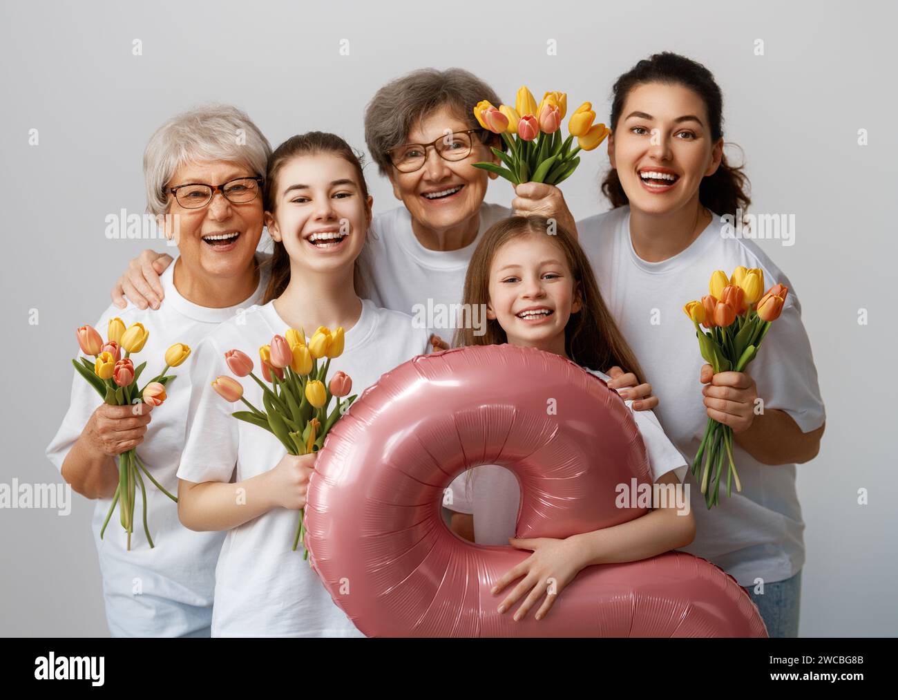 Happy women's day! Children daughters are congratulating mom and grandmothers giving them flowers tulips. Grannys, mom and girls smiling on light grey Stock Photo