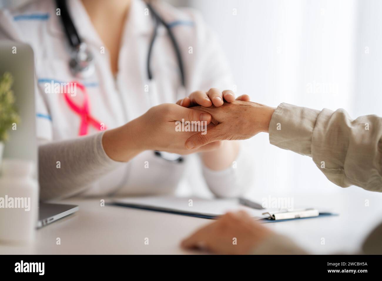Pink ribbon for breast cancer awareness. Female patient listening to doctor in medical office. Support people living with tumor illness. Stock Photo