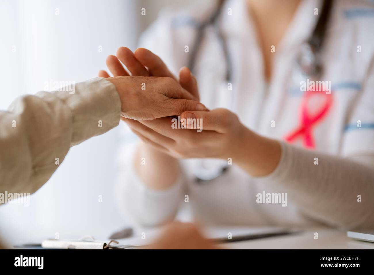Pink ribbon for breast cancer awareness. Female patient listening to doctor in medical office. Support people living with tumor illness. Stock Photo
