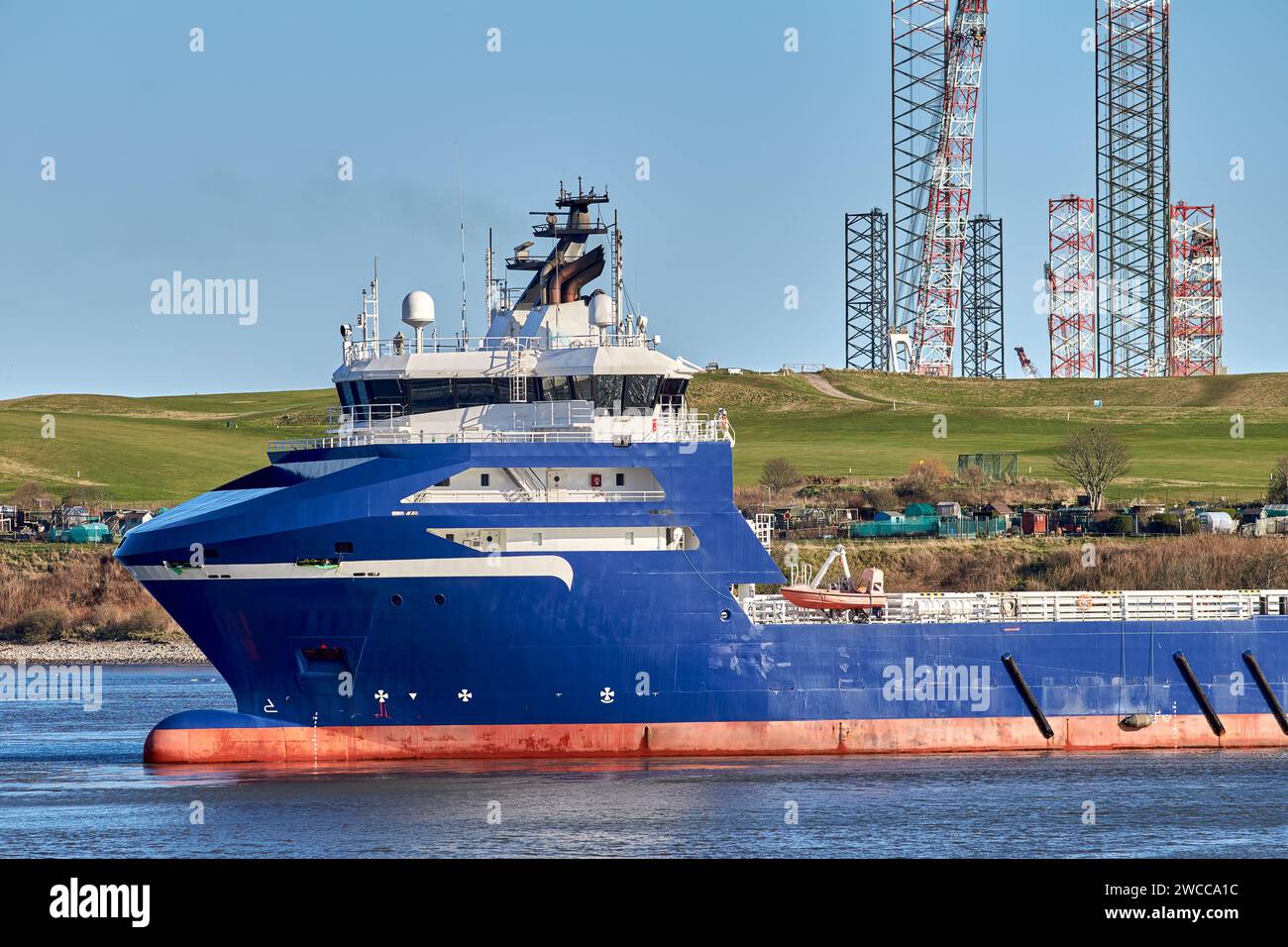Blue platform supply vessel navigating in port with mountains on the