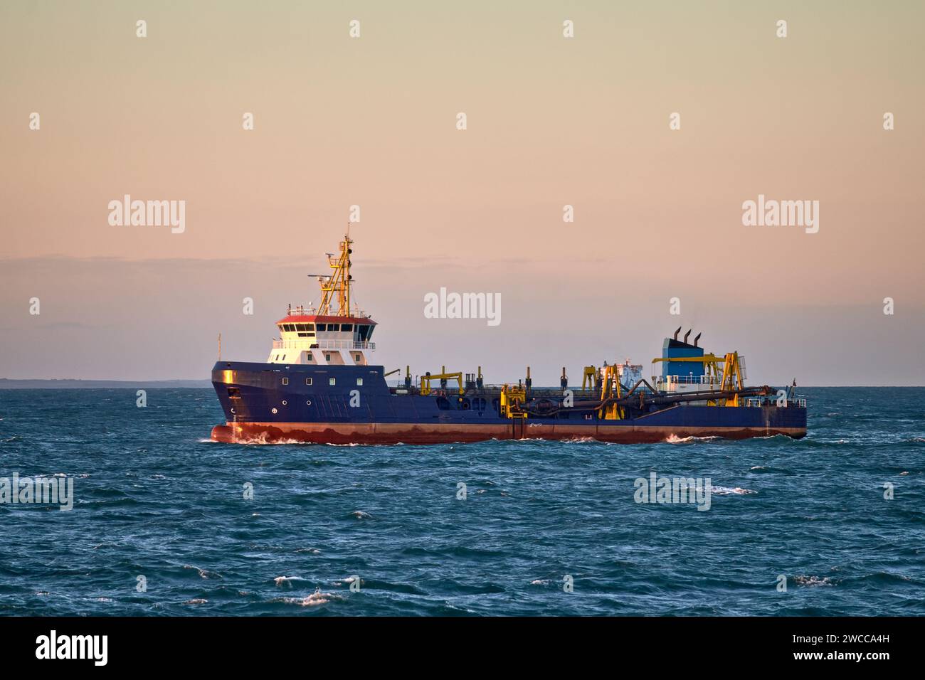 Dredger vessel working in the sea, near the coast on a sunny day. Stock Photo