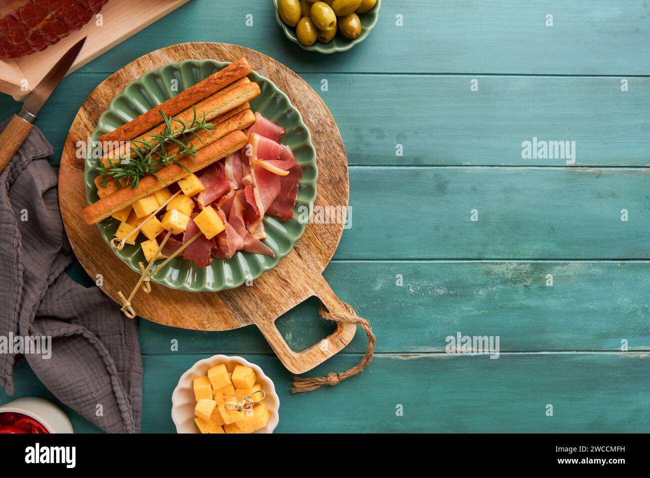 Slices of prosciutto or jamon. Antipasto Delicious grissini sticks with prosciutto, cheese, rosemary, olives on green plate on old wooden blue backgro Stock Photo
