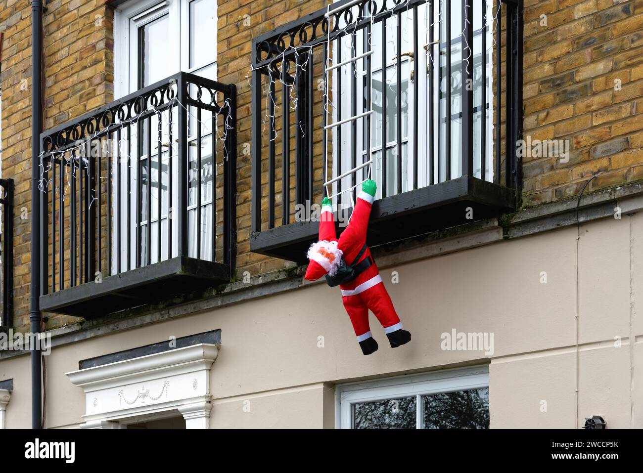 A blow-up Father Christmas hanging off an apartment balcony as if trying to climb up ladder to gain access to the premises, Surrey England UK Stock Photo