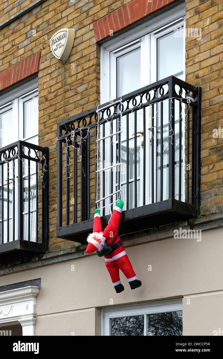 A blow-up Father Christmas hanging off an apartment balcony as if trying to climb up ladder to gain access to the premises, Surrey England UK Stock Photo