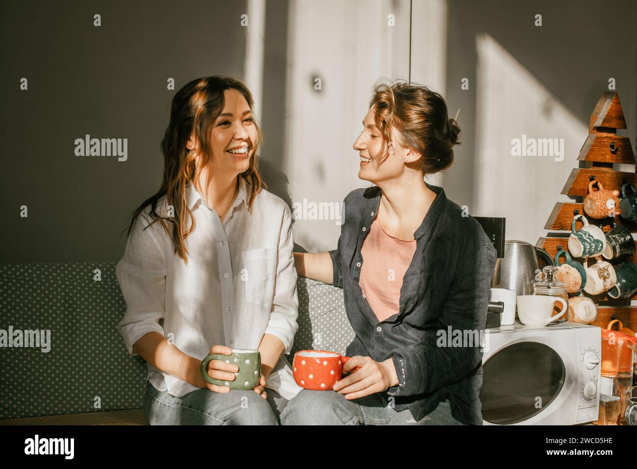 Time for intimate conversations: two women drinking tea in the sunshine in a cozy environment Girls friends talking over a cup of coffee Stock Photo