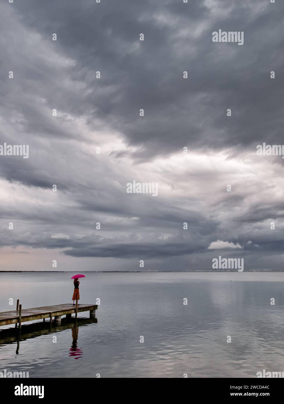 Girl with pink umbrella on a lake pier on a cloudy and raining day, in the Albufera natural park, Valencia, Spain Stock Photo