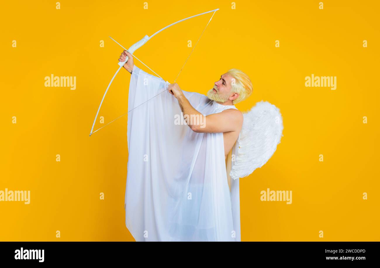 Male cupid in angel wings at valentines day with bow and arrow. God of love. Valentine angel shooting arrow of love. Smiling bearded man in angel Stock Photo