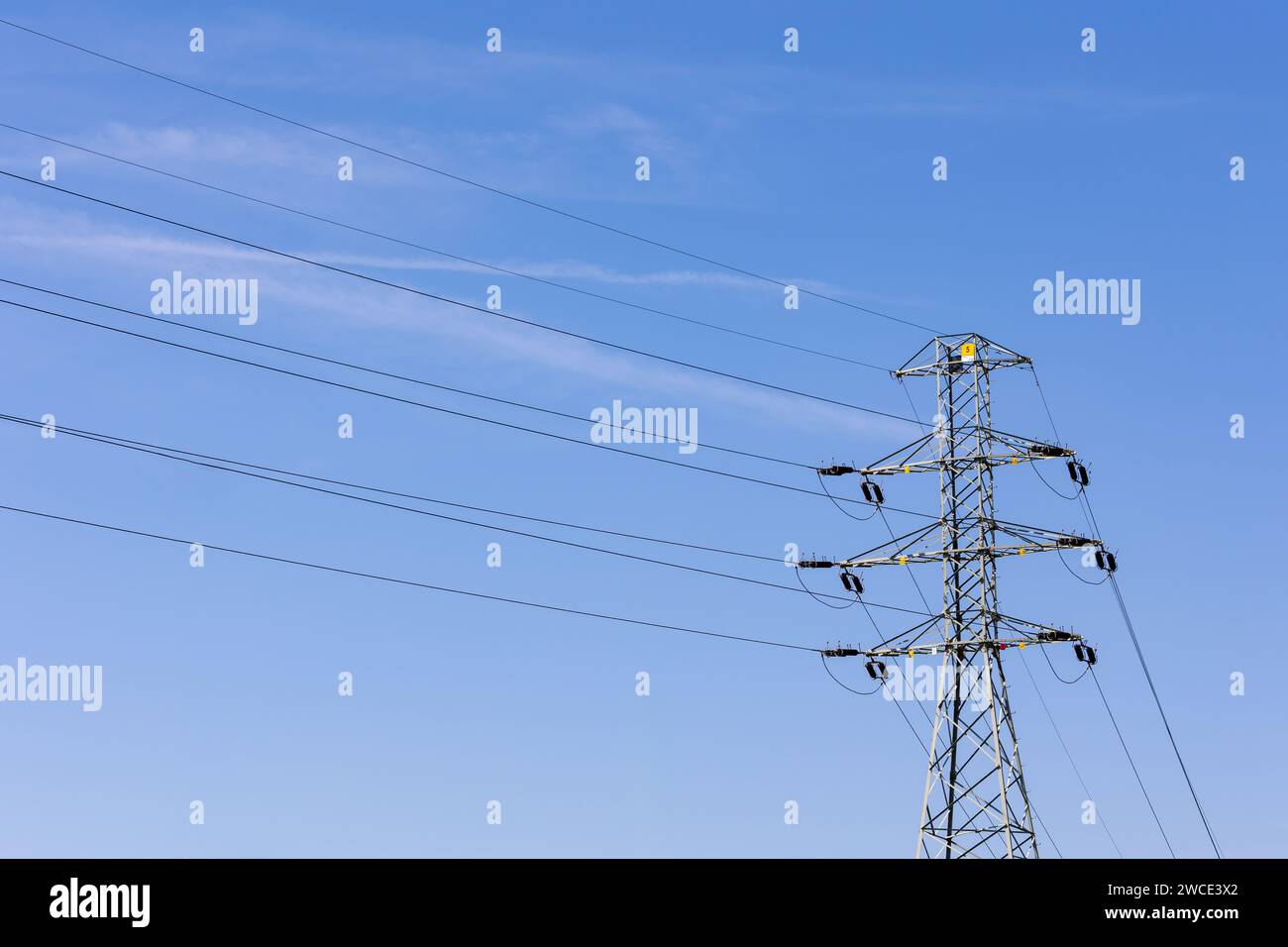 High voltage poles and high voltage cables against the background of the blue sky. Supply of electricity using overhead lines. Stock Photo